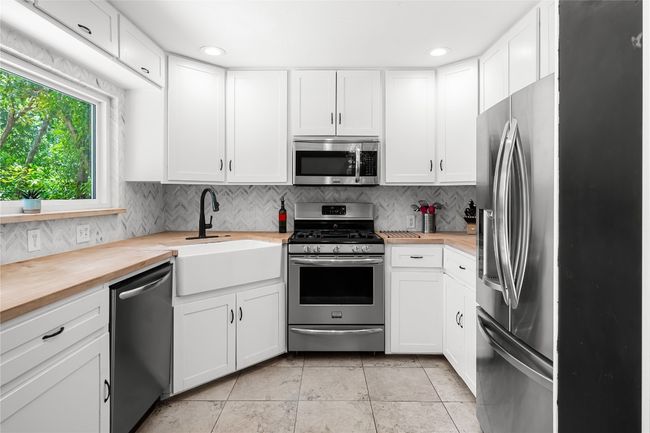 Kitchen with huge picture window, stainless appliances, white cabinetry and butcher block style countertops. | Image 5