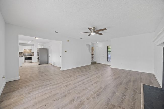 Unfurnished living room with ceiling fan, a textured ceiling, visible vents, and light wood-style flooring | Image 6
