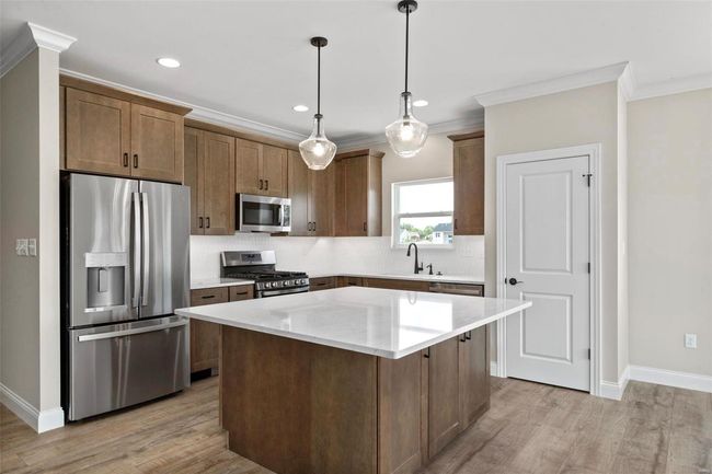 Kitchen with decorative light fixtures, a kitchen island, light wood-type flooring, and stainless steel appliances | Image 13