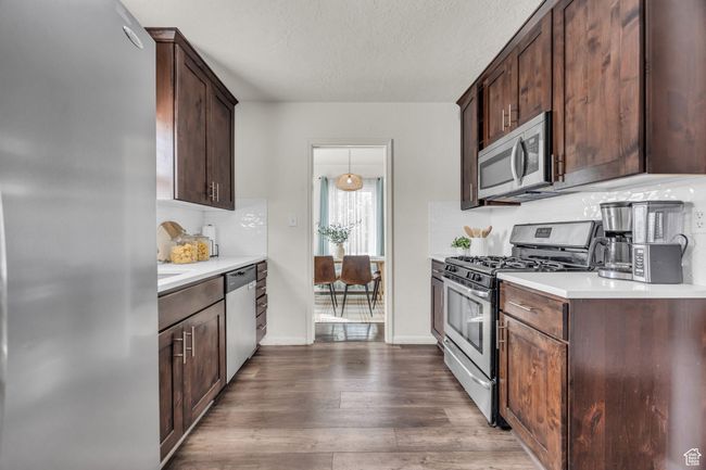 Kitchen featuring appliances with stainless steel finishes, light countertops, dark wood-type flooring, dark brown cabinets, and a textured ceiling | Image 10