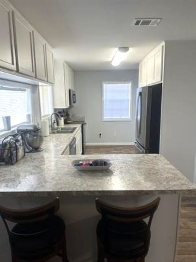 Kitchen with freestanding refrigerator, a kitchen bar, a peninsula, visible vents, and a sink | Image 7