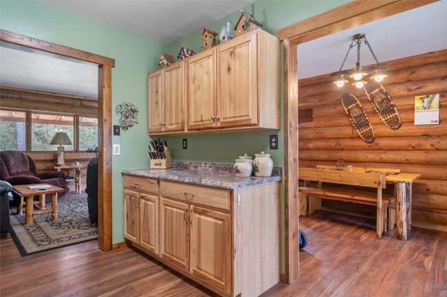 Kitchen featuring rustic walls, dark wood finished floors, light brown cabinets, light countertops, and pendant lighting | Image 40