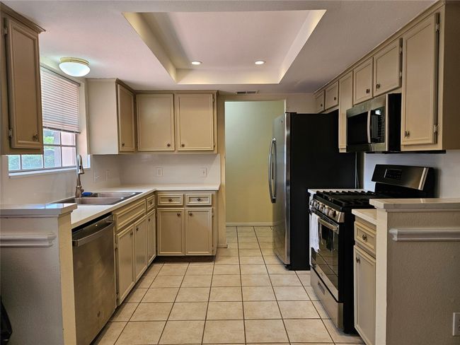 Kitchen with appliances with stainless steel finishes, a raised ceiling, light countertops, light tile patterned flooring, and recessed lighting | Image 8