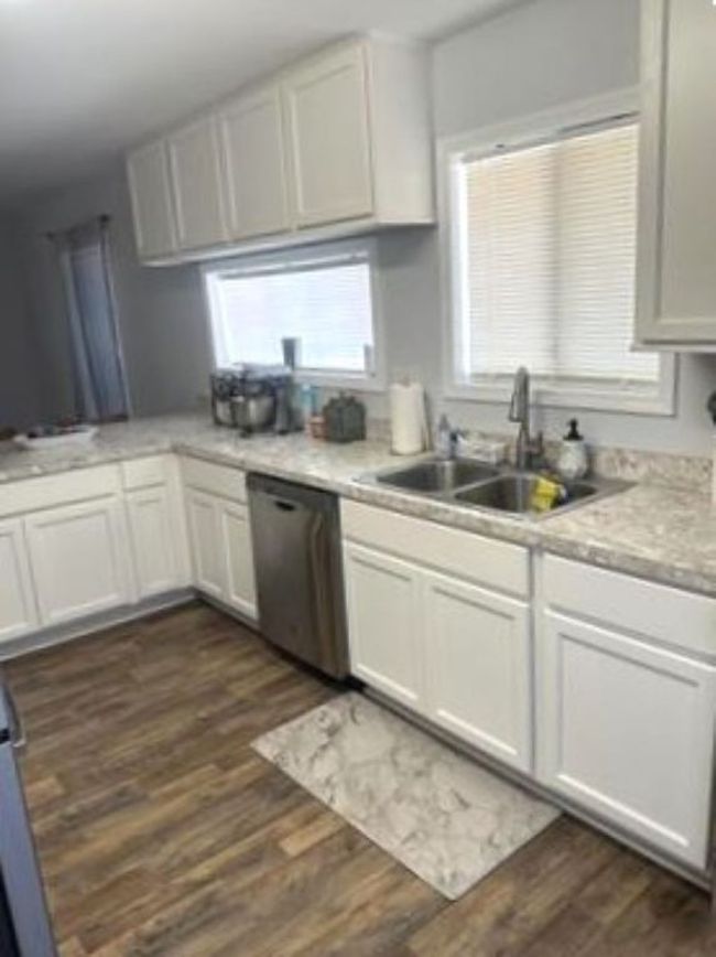 Kitchen with light countertops, white cabinetry, dark wood-type flooring, stainless steel dishwasher, and a sink | Image 5