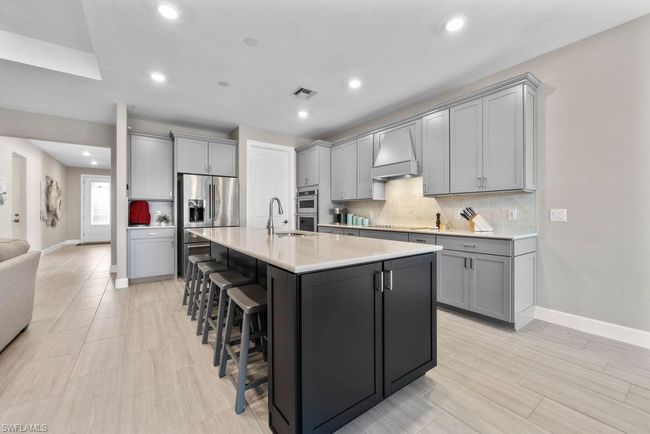 Kitchen featuring tasteful backsplash, a kitchen bar, gray cabinets, custom exhaust hood, and stainless steel appliances | Image 28
