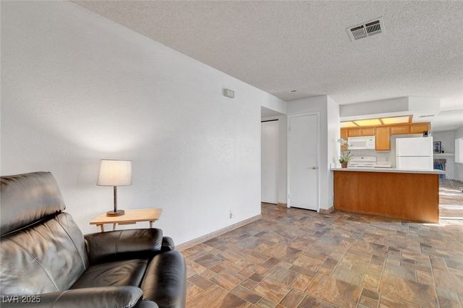 Living area featuring a textured ceiling, stone finish flooring, baseboards, and visible vents | Image 5