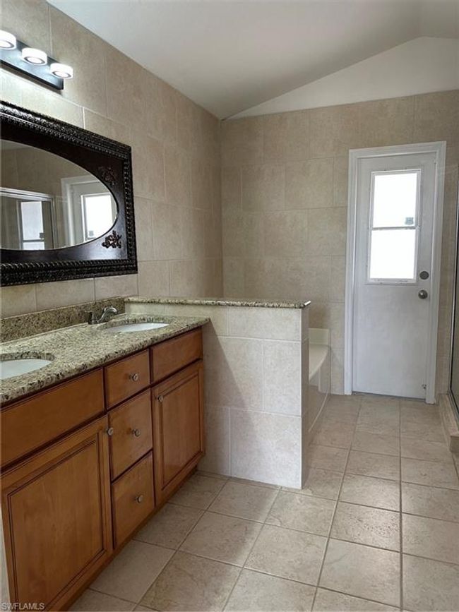 Full bathroom featuring tile walls, lofted ceiling, double vanity, a garden tub, and a stall shower | Image 16