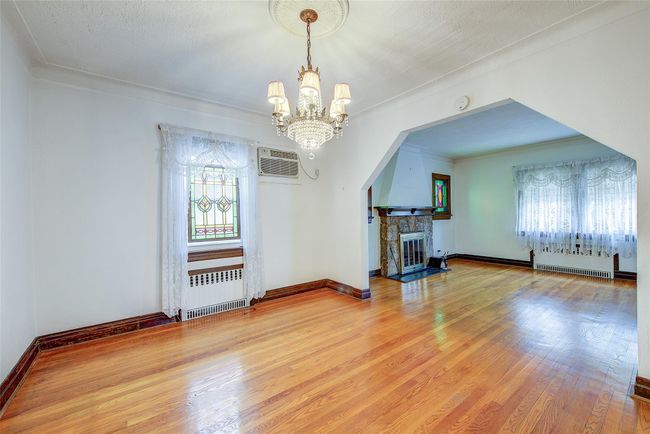 Living area featuring radiator, a chandelier, a wall mounted AC, wood finished floors, and crown molding | Image 7