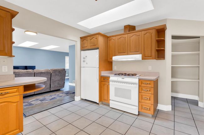 Kitchen with light countertops, a skylight, white appliances, under cabinet range hood, and light tile patterned floors | Image 29