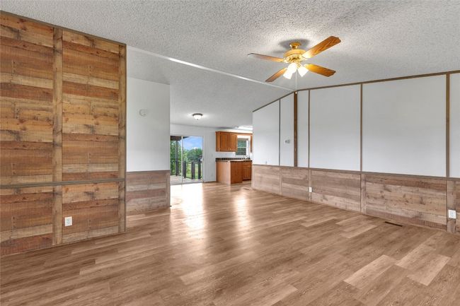 Unfurnished living room with ceiling fan, a textured ceiling, light wood-style floors, a wainscoted wall, and wood walls | Image 11