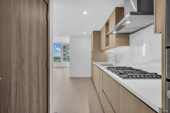 Kitchen with wall chimney exhaust hood, stainless steel gas cooktop, light countertops, modern cabinets, and recessed lighting | Image 4