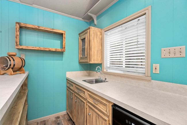 This cozy wet bar features turquoise walls and rustic wood cabinetry, complemented by a small sink and ample amount of natural lighting. The space over looks the pool area in the backyard. | Image 22