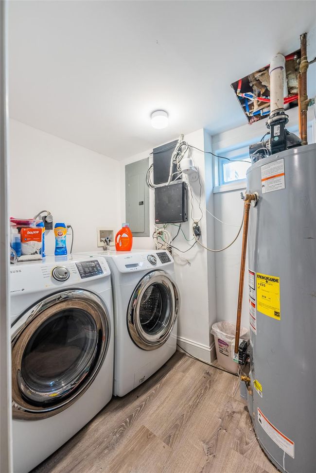 Laundry area featuring gas water heater, washing machine and clothes dryer, light wood-style flooring, and electric panel | Image 36