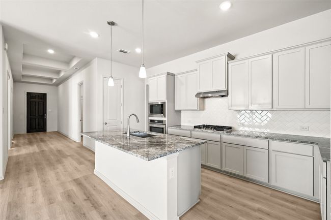 Kitchen featuring appliances with stainless steel finishes, recessed lighting, light stone countertops, tasteful backsplash, and under cabinet range hood | Image 7