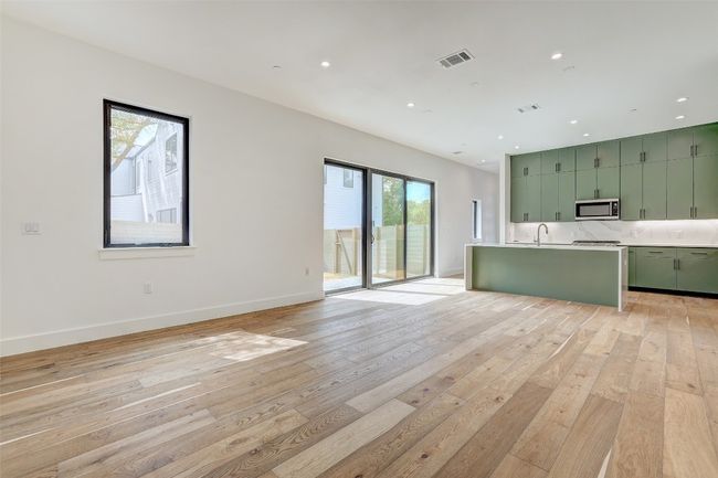 Kitchen with green cabinets, light wood-type flooring, light countertops, stainless steel microwave, and open floor plan | Image 15