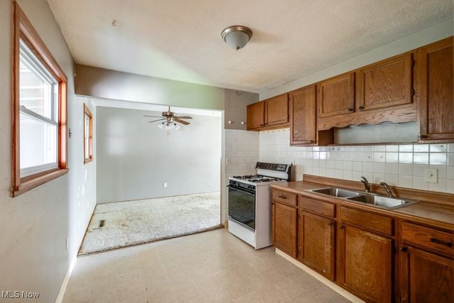 Kitchen with white gas stove, a sink, brown cabinets, light floors, and a textured ceiling | Image 16