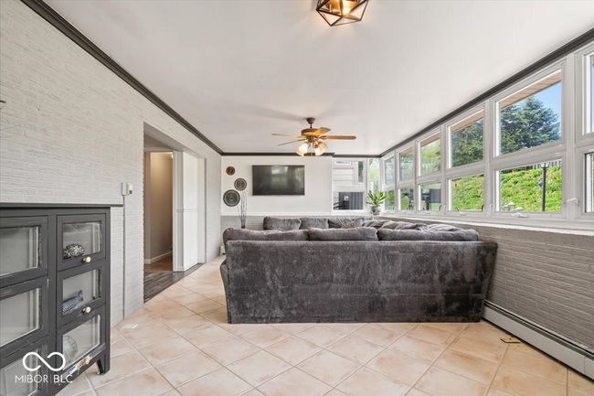 living area with a baseboard radiator, ceiling fan, light tile patterned floors, brick wall, and crown molding | Image 11