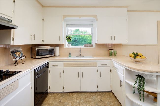 Kitchen with a sink, black appliances, tile countertops, under cabinet range hood, and white cabinets | Image 7