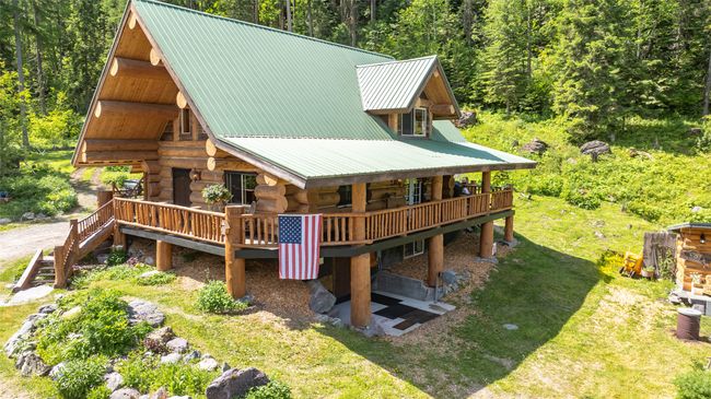 Back of house featuring log exterior, a view of trees, a wooden deck, and a lawn | Image 66