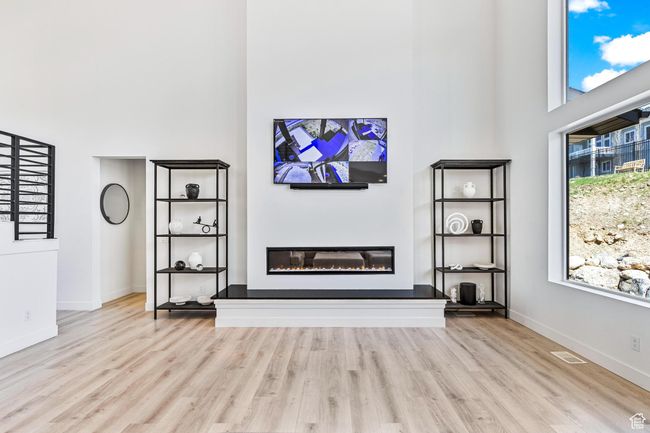 Unfurnished living room featuring baseboards, wood finished floors, a glass covered fireplace, and a towering ceiling | Image 18