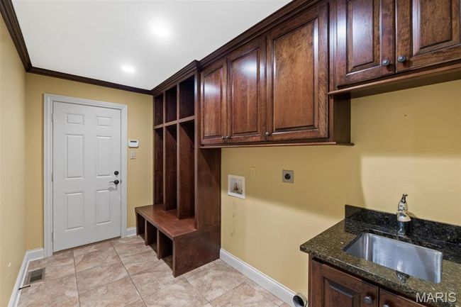 Laundry area with electric dryer hookup, cabinet space, washer hookup, crown molding, and light tile patterned flooring | Image 25