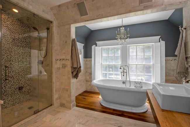 Full bathroom featuring tile walls, a soaking tub, a chandelier, a shower stall, and wainscoting | Image 29