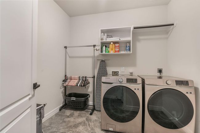 Modern appliances, ample shelving for storage, a hanging rod, and a convenient ironing station, all set on stylish tile flooring. | Image 19