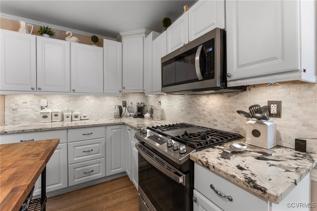 Kitchen with backsplash, crown molding, white cabinets, stainless steel appliances, and wood counters | Image 14