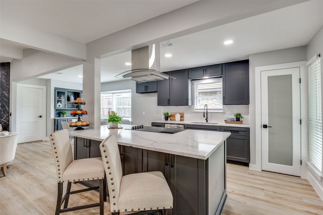 Kitchen with island exhaust hood, light stone counters, light wood-style floors, a kitchen breakfast bar, and recessed lighting | Image 12