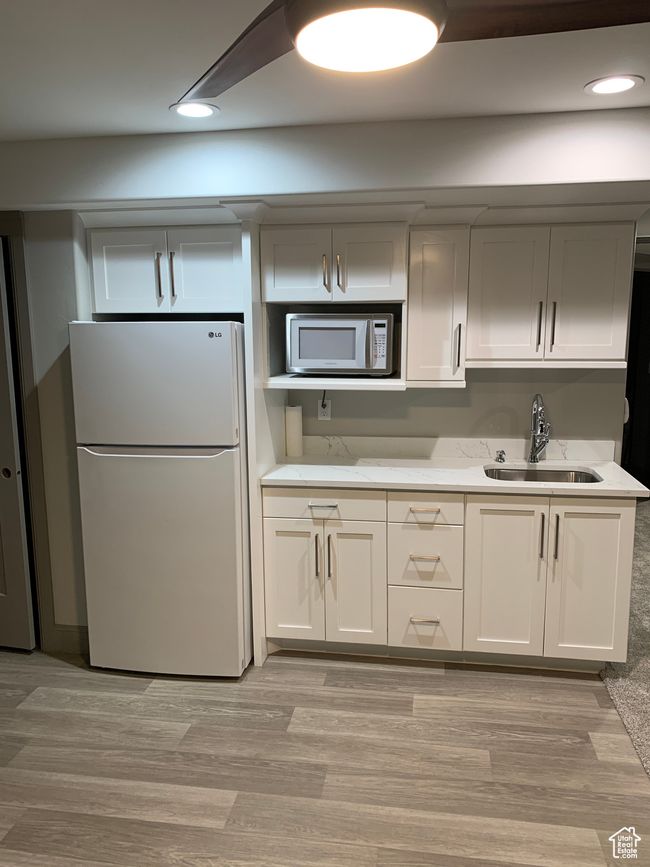 Kitchen featuring light wood finished floors, white appliances, a sink, and recessed lighting | Image 17