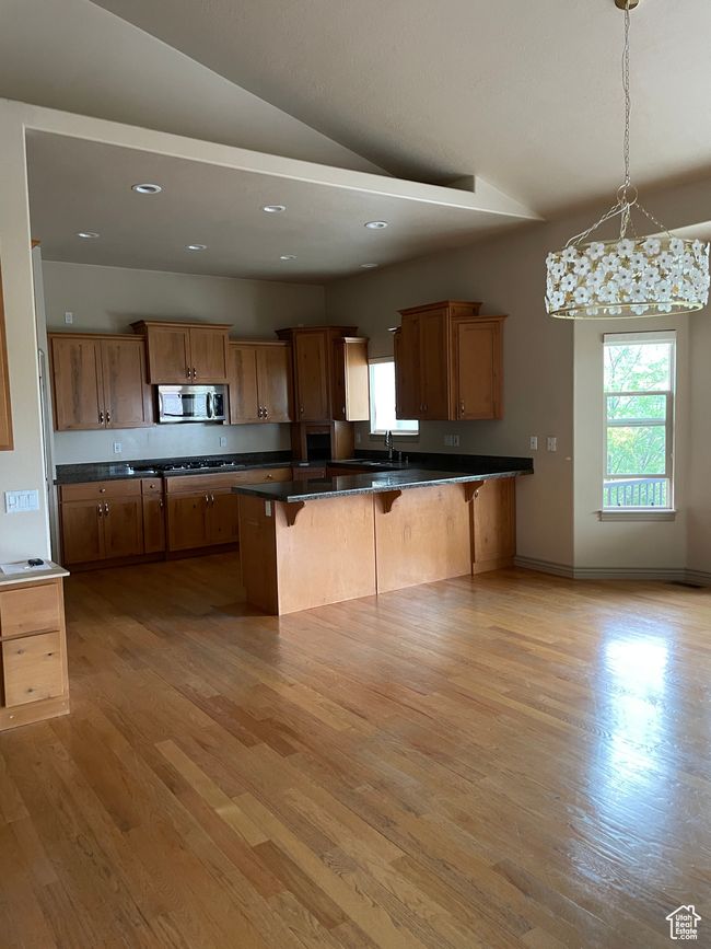 Kitchen with stainless steel microwave, a breakfast bar area, dark countertops, lofted ceiling, and light wood-type flooring | Image 8