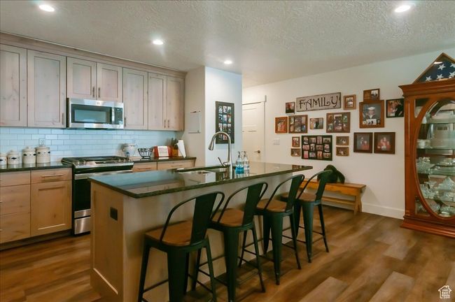 Kitchen with appliances with stainless steel finishes, a sink, dark countertops, dark wood-style flooring, and decorative backsplash | Image 8