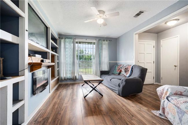 Living area featuring ceiling fan, a textured ceiling, baseboards, wood finished floors, and visible vents | Image 7