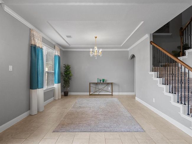 This spacious and elegant entryway features neutral tile flooring, a stylish staircase with wrought-iron railings, and a beautiful chandelier. Arched doorways lead to an open living area and dining space, creating a welcoming atmosphere. | Image 20