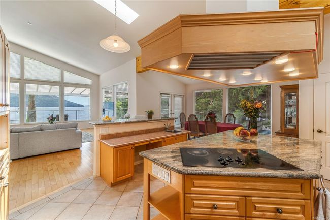 Kitchen featuring black electric cooktop, vaulted ceiling, light tile patterned floors, a skylight, and custom exhaust hood | Image 16