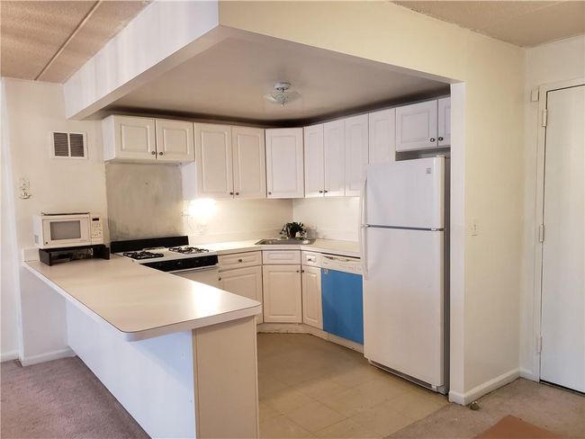 Kitchen with white appliances, sink, kitchen peninsula, and white cabinets | Image 4