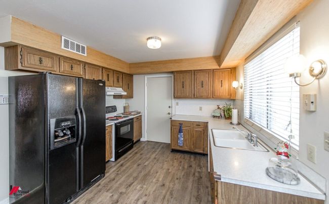 Kitchen with a sink, black fridge, range with electric stovetop, under cabinet range hood, and visible vents | Image 13