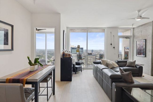 Living area with a ceiling fan, light wood finished floors, floor to ceiling windows, and a view of city | Image 13