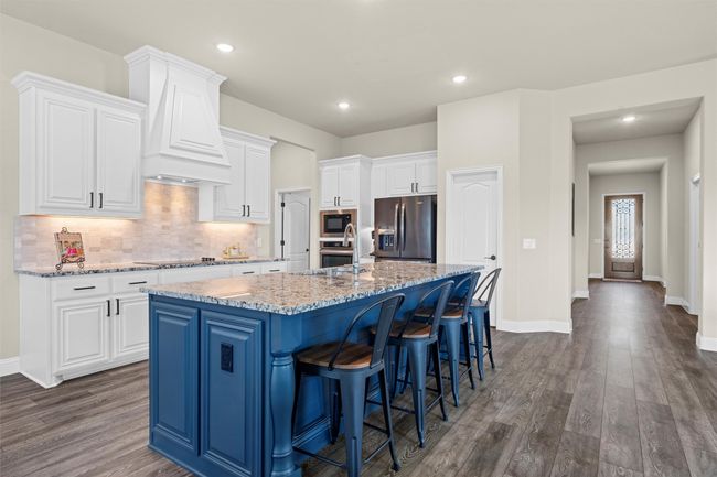 Kitchen featuring black appliances, premium range hood, a kitchen island with sink, white cabinetry, and dark wood-type flooring | Image 8