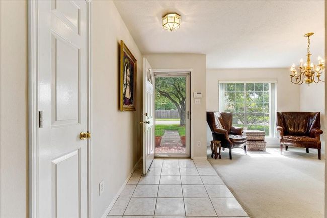 Bright entryway with tiled flooring, leading to a cozy living area featuring large windows. The door opens to a green, tree-lined view, providing plenty of natural light. | Image 5