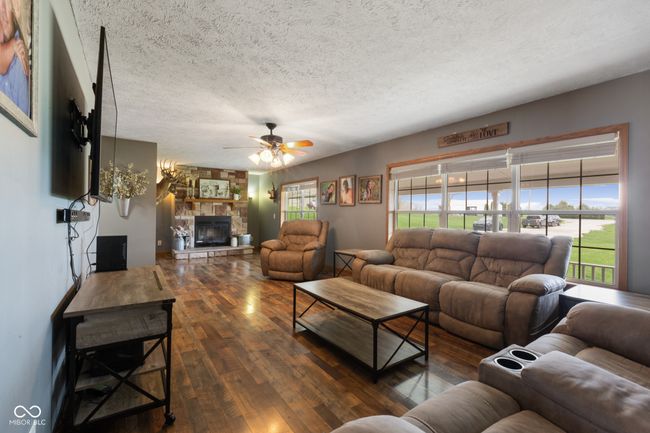 living room with wood-type flooring, a ceiling fan, a fireplace, and a textured ceiling | Image 11