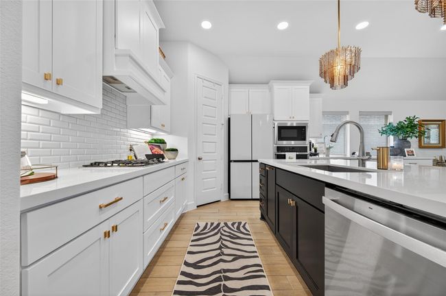 Gourmet kitchen with shaker-style cabinetry, subway tile backsplash, and quartz countertops. Features include a spacious center island with undermount sink, gas cooktop, built-in microwave, and modern stainless steel appliances. | Image 11