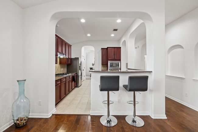 Kitchen featuring dark brown cabinets, appliances with stainless steel finishes, dark stone countertops, a kitchen breakfast bar, and decorative backsplash | Image 16