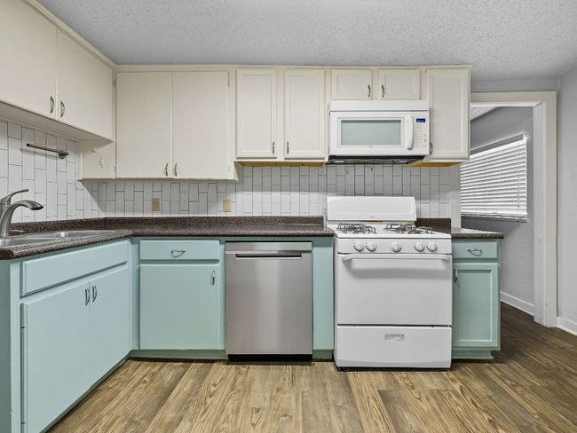 Kitchen featuring white appliances, dark countertops, light wood-style floors, decorative backsplash, and a textured ceiling | Image 17