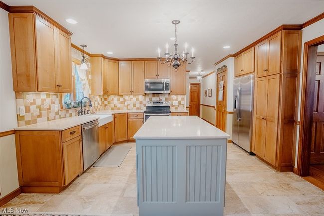 Main kitchen featuring stainless steel appliances, a chandelier, a center island, light countertops, and pendant lighting | Image 6