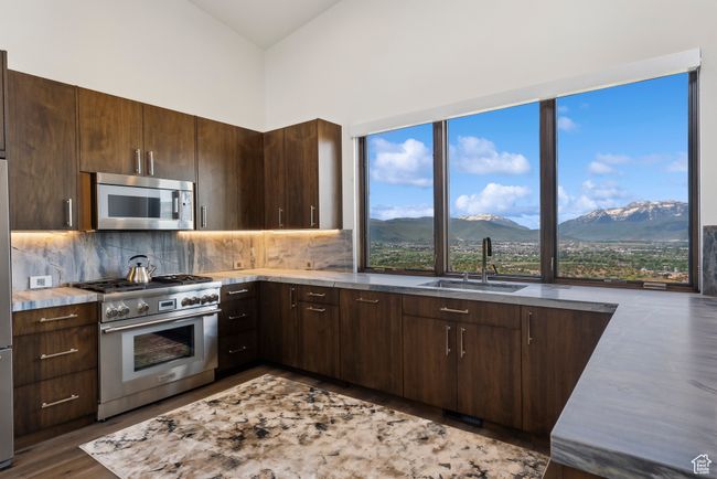 Kitchen featuring appliances with stainless steel finishes, a sink, a mountain view, dark brown cabinetry, and backsplash | Image 92