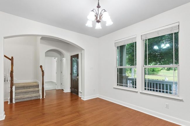 Spare room featuring dark wood finished floors, a chandelier, stairs, baseboards, and arched walkways | Image 6