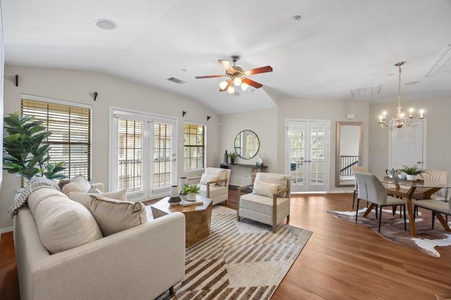 Living area featuring a chandelier, vinyl wood floors, high ceiling, with ceiling fan, and French doors leading out to balcony. | Image 6
