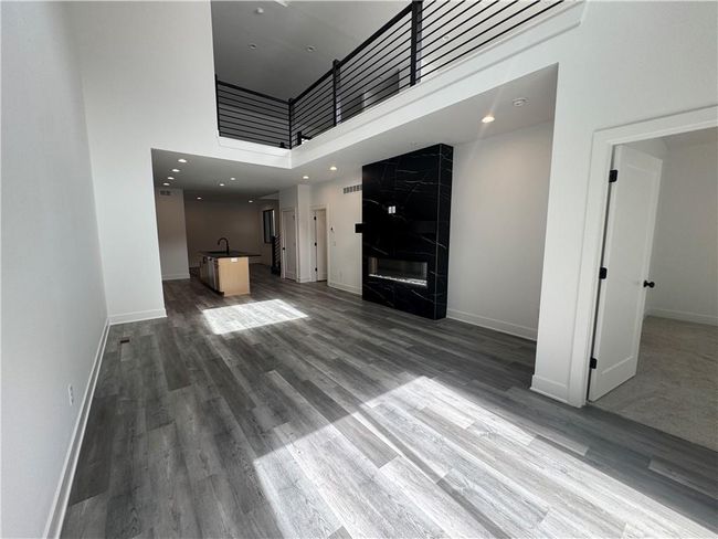Unfurnished living room with a high ceiling, a sink, baseboards, and wood finished floors | Image 7