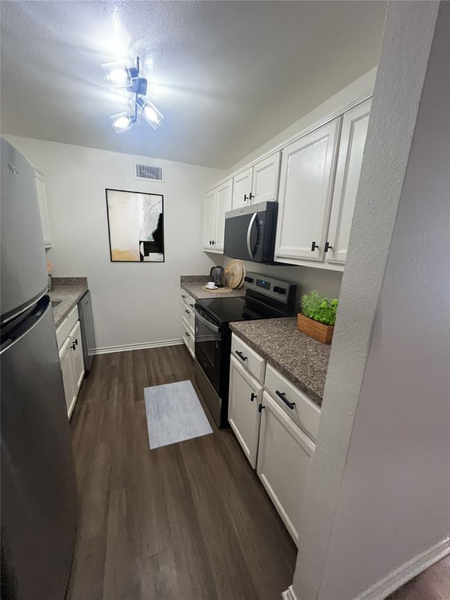 Kitchen featuring white cabinets, appliances with stainless steel finishes, baseboards, visible vents, and dark wood-style floors | Image 5